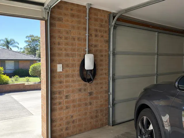 Wall-mounted EV charger on a brick garage wall beside a closed garage door in Berkeley Vale